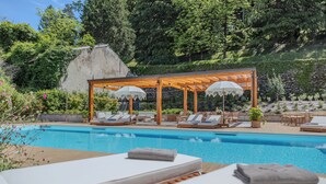 A pool area with lounge chairs and umbrellas, surrounded by greenery and a stone wall. - Appartamento Il Borgo (Bellagio)