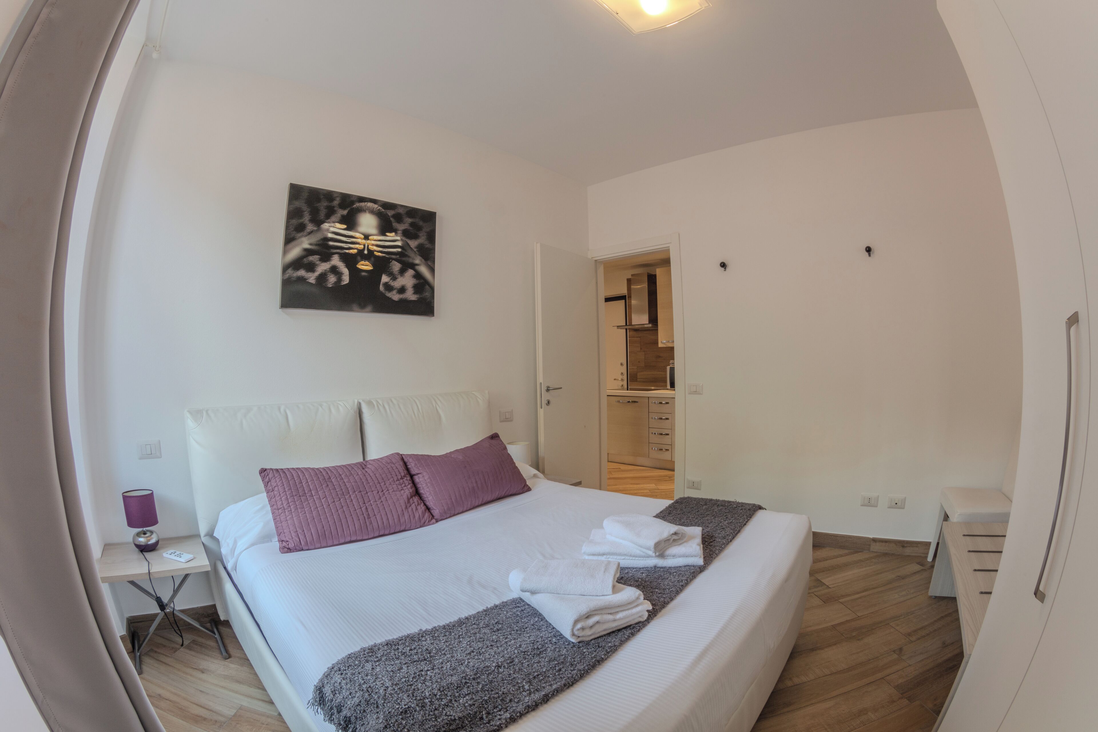 Un dormitorio con cama, mesita de noche, una obra de arte en la pared y un vestidor.
