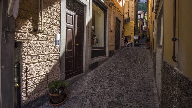 A narrow cobblestone street flanked by buildings with stone facades and wooden doors. - Appartamento Il Borgo (Bellagio)