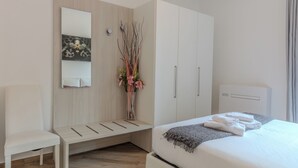 A modern bedroom with a bed, a bedside table, a chair, a wardrobe, a mirror, and a vase with flowers. - Appartamento Il Borgo (Bellagio)