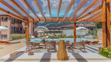 A covered outdoor area with lounge chairs and a pool.