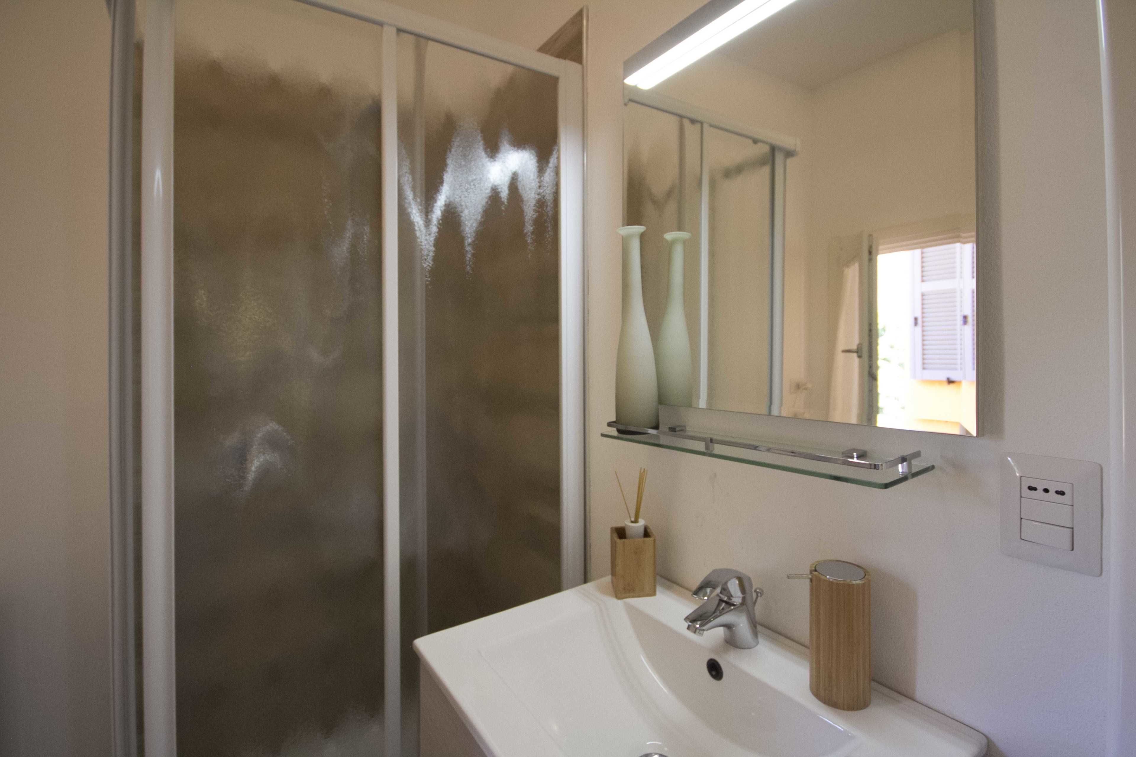 Un baño con cabina de ducha de vidrio, un lavamanos blanco con grifo moderno y un espejo sobre el lavamanos.
