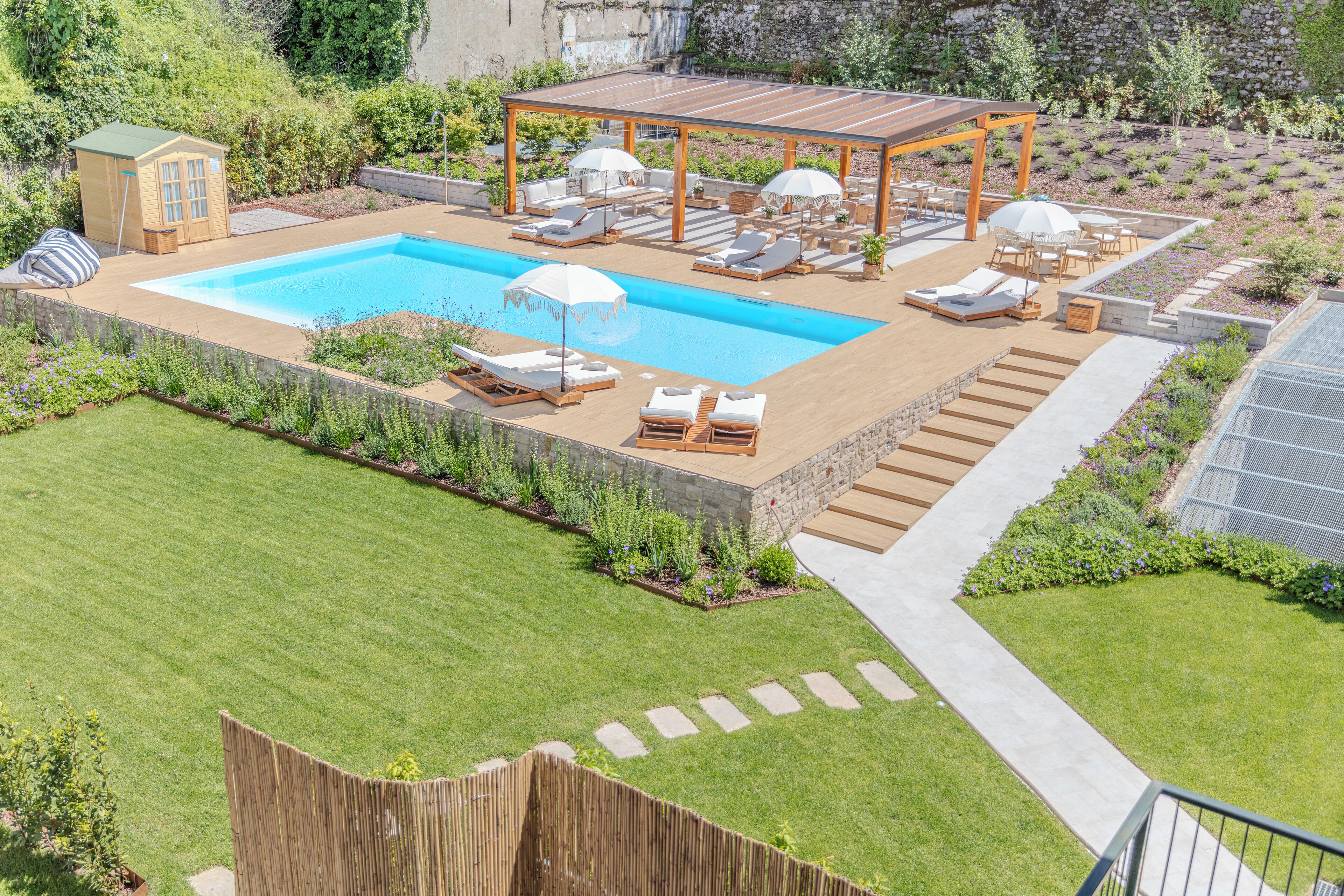 Un jardin avec une piscine, des chaises longues, une pergola et un petit abri de jardin.