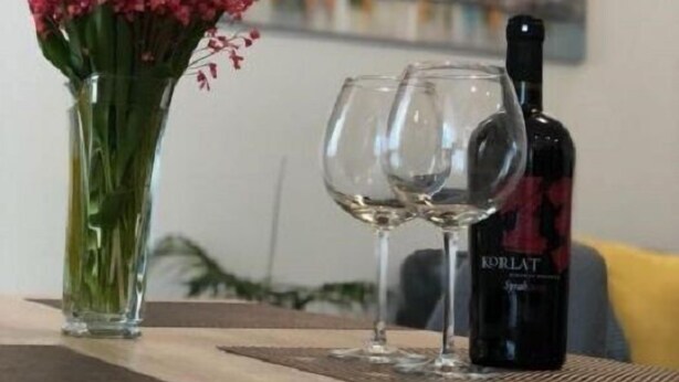 Een eettafel met een fles wijn, twee wijnglazen en een bloevas.