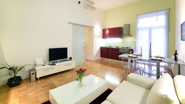 Uma sala de estar moderna com uma TV de tela plana, um sofá branco e uma mesa de centro com um vaso de flores.