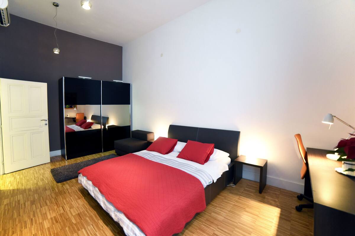 A modern bedroom with a large bed, a wardrobe, a desk, and a chair.