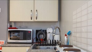 Een keuken met een magnetron, koffiezetapparaat en een spoelbak met een kraan.