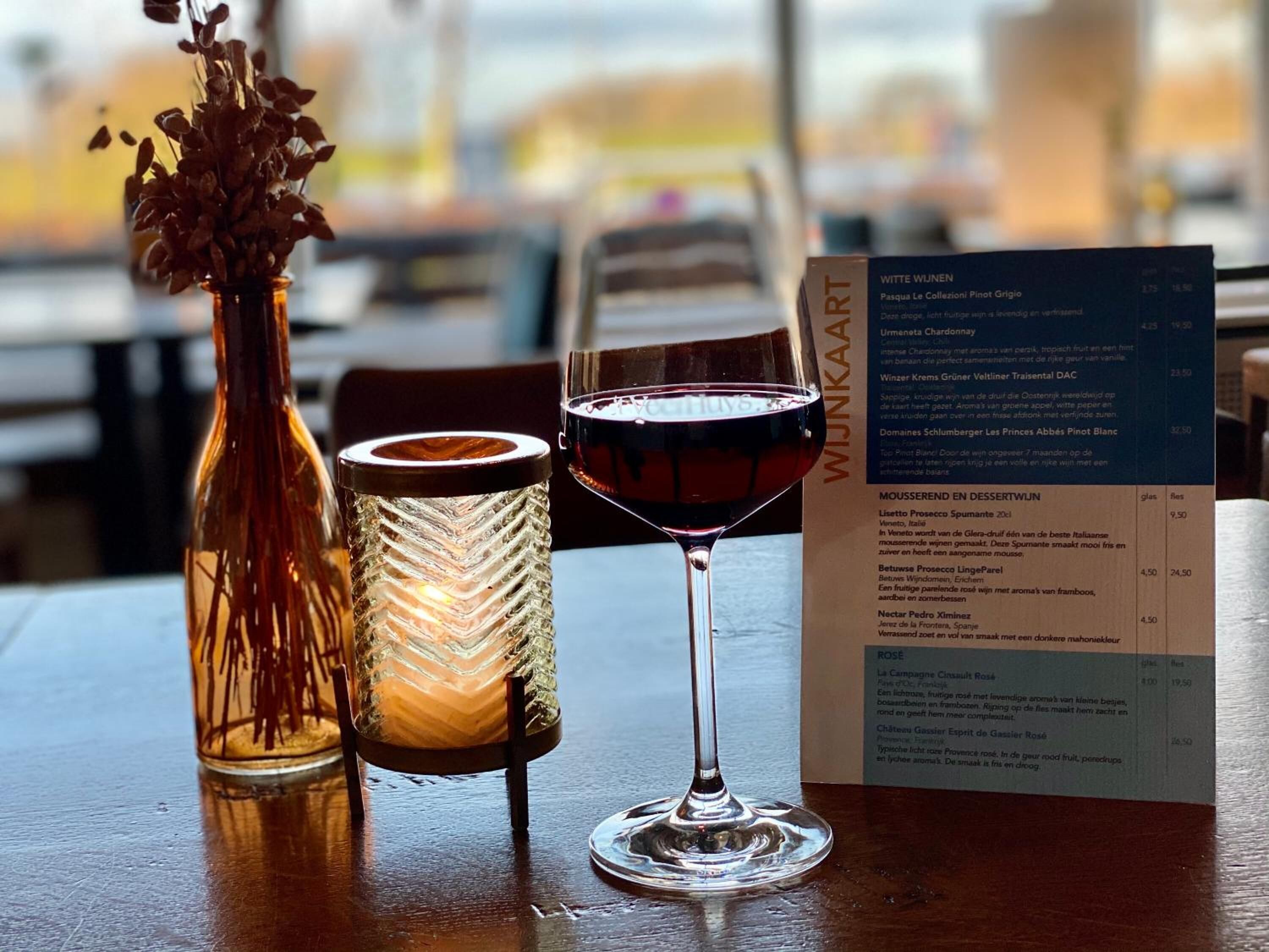 Une table avec une bougie, un verre de vin rouge et un menu.