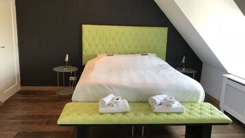 A neatly made bed with a green headboard and footboard, a small bedside table, and a bench with towels.