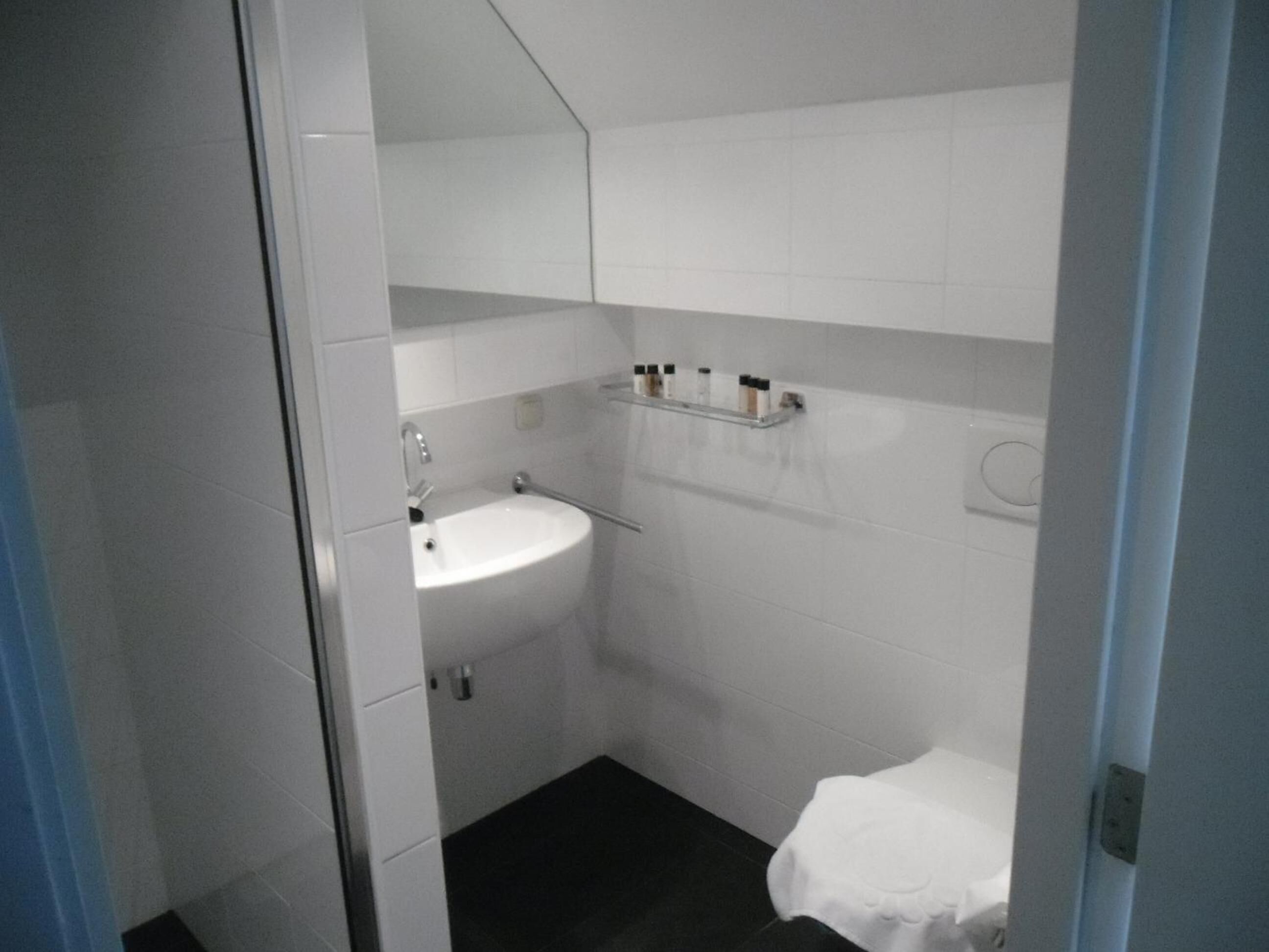 A small bathroom with a white sink, a mirror, and a shelf with toiletries.
