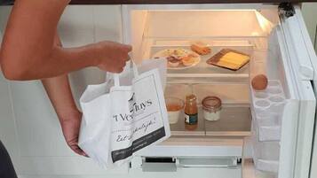 A person opening a refrigerator door in a kitchen, revealing food items and a shopping bag inside.