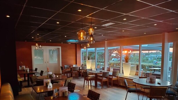 Un restaurante espacioso con suelo de madera, varias mesas y sillas, y ventanas amplias que ofrecen vistas al exterior.