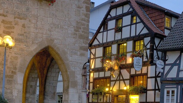 A traditional half-timbered building with a stone archway, a reflection in the water, and a sign indicating a hotel. - Hotel Goldflair am Rathaus (Korbach)