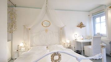 A white four-poster bed with a canopy, bedside tables with lamps, a small desk, and a chair.