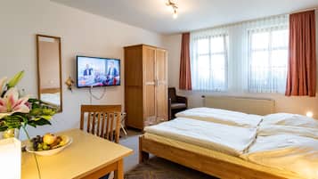Habitación de hotel con una cama de madera, un escritorio con frutero, televisor, armario y ventana con cortinas.