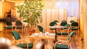 Ein Restaurant mit Holztischen und grünen Stühlen, einer großen Topfpflanze und einer traditionellen japanischen Schiebetür im Hintergrund.