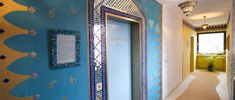 A hallway with a blue and gold patterned wall, a door labeled "Dresches Colts 27", and a small framed notice.