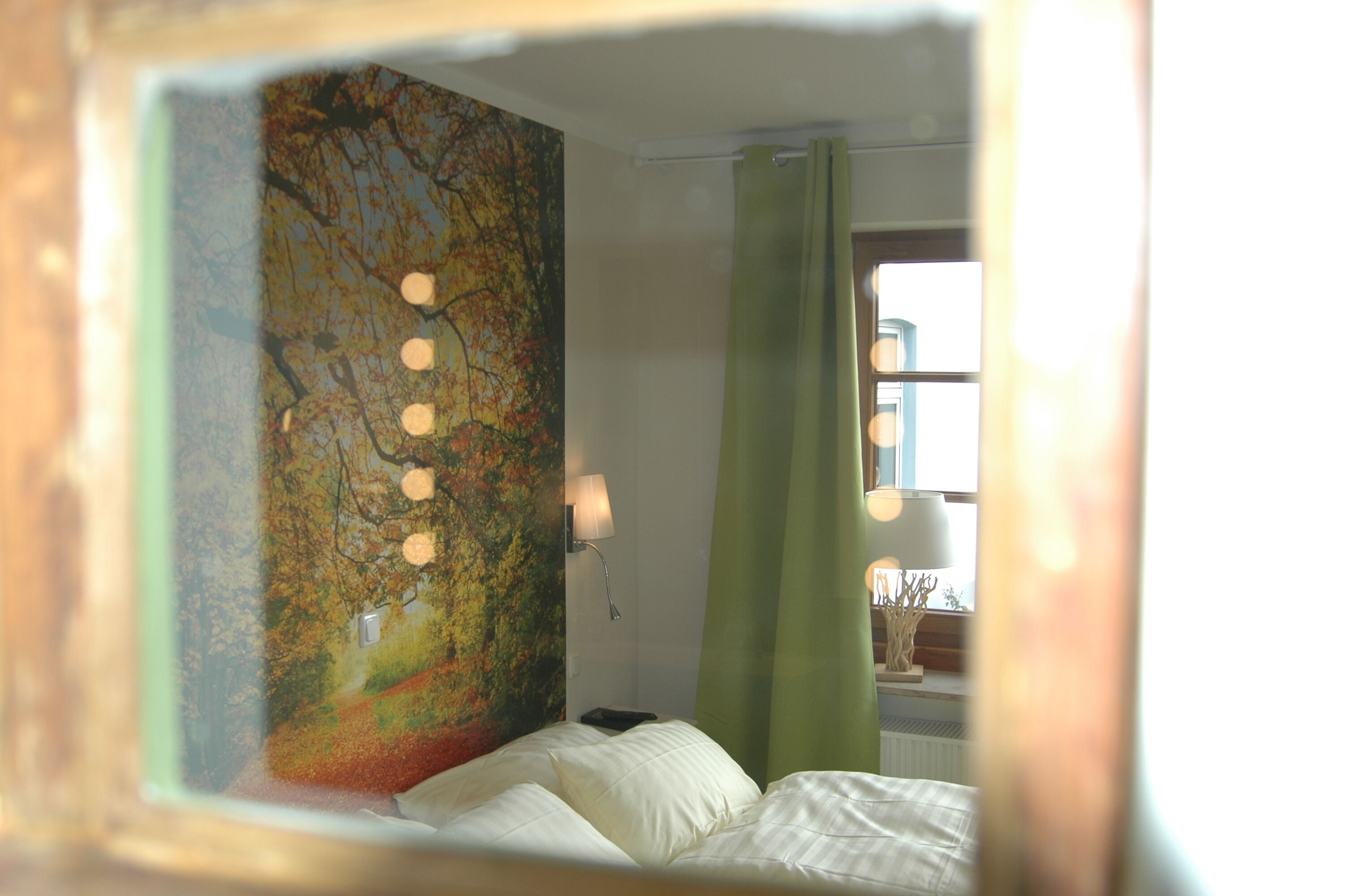 Un dormitorio con cama, mesita de noche, lámpara, ventana con cortinas y un cuadro en la pared.