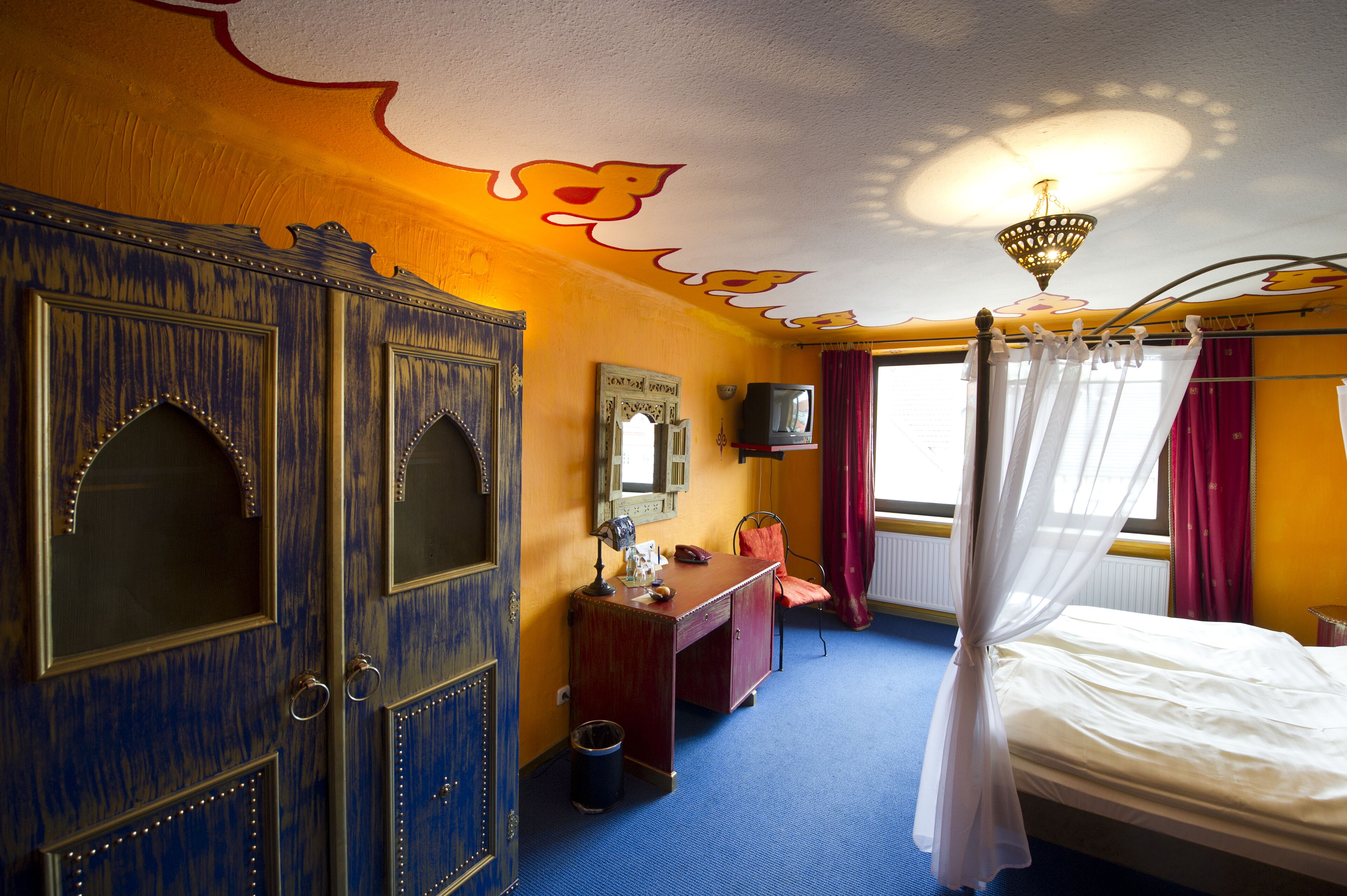 Een kamer met een bed, bureau, kledingkast en televisie.