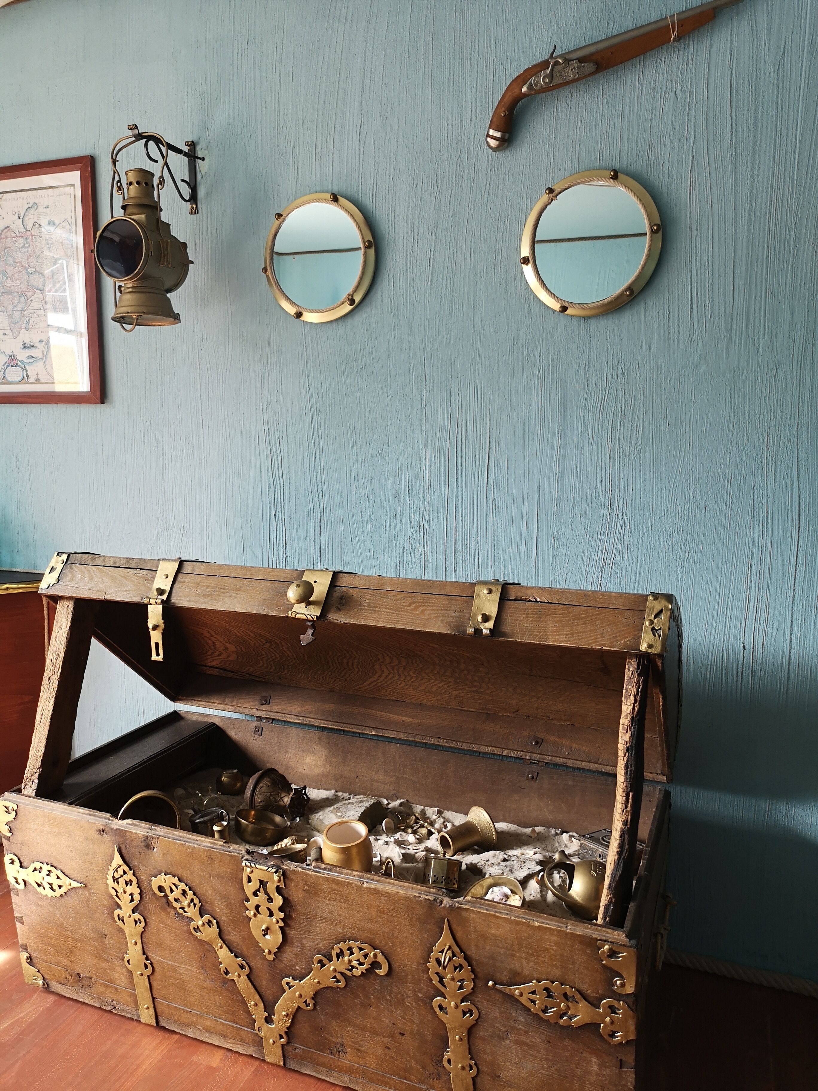 Un cofre de madera con detalles metálicos ornamentales, dos espejos colgados en la pared y un farol antiguo.