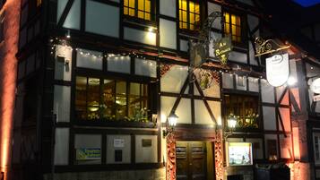 Un bâtiment traditionnel à colombages, avec des fenêtres illuminées et une enseigne indiquant qu’il s’agit d’un hôtel.