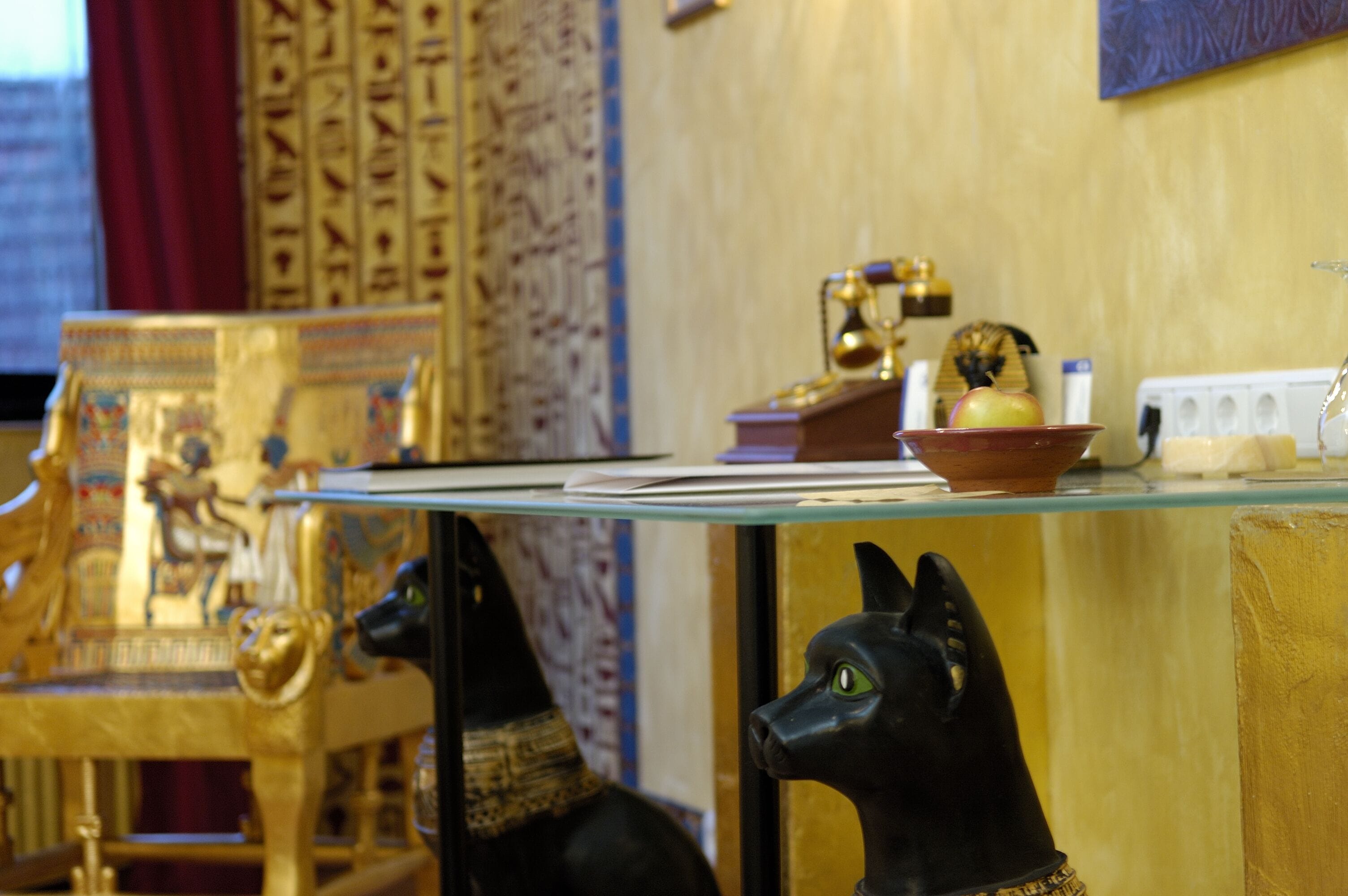 A room with a glass table displaying Egyptian artifacts, including a golden chair and a black statue of an Egyptian deity.