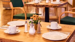 A dining area with wooden tables, chairs, and a variety of tableware. - Hotel Goldflair am Rathaus (Korbach)