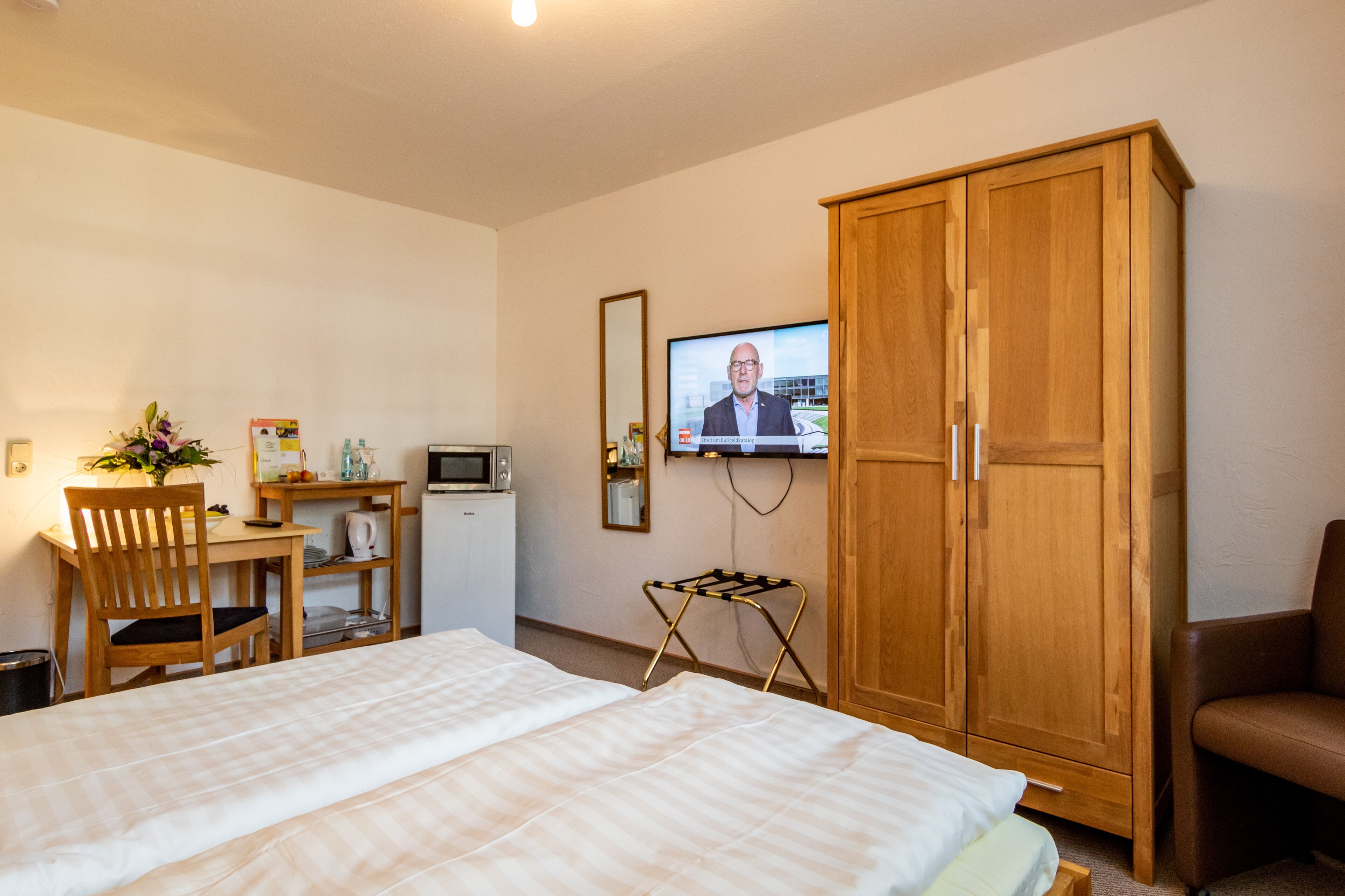 A hotel room with a bed, a desk with a computer, a television, and a wardrobe.