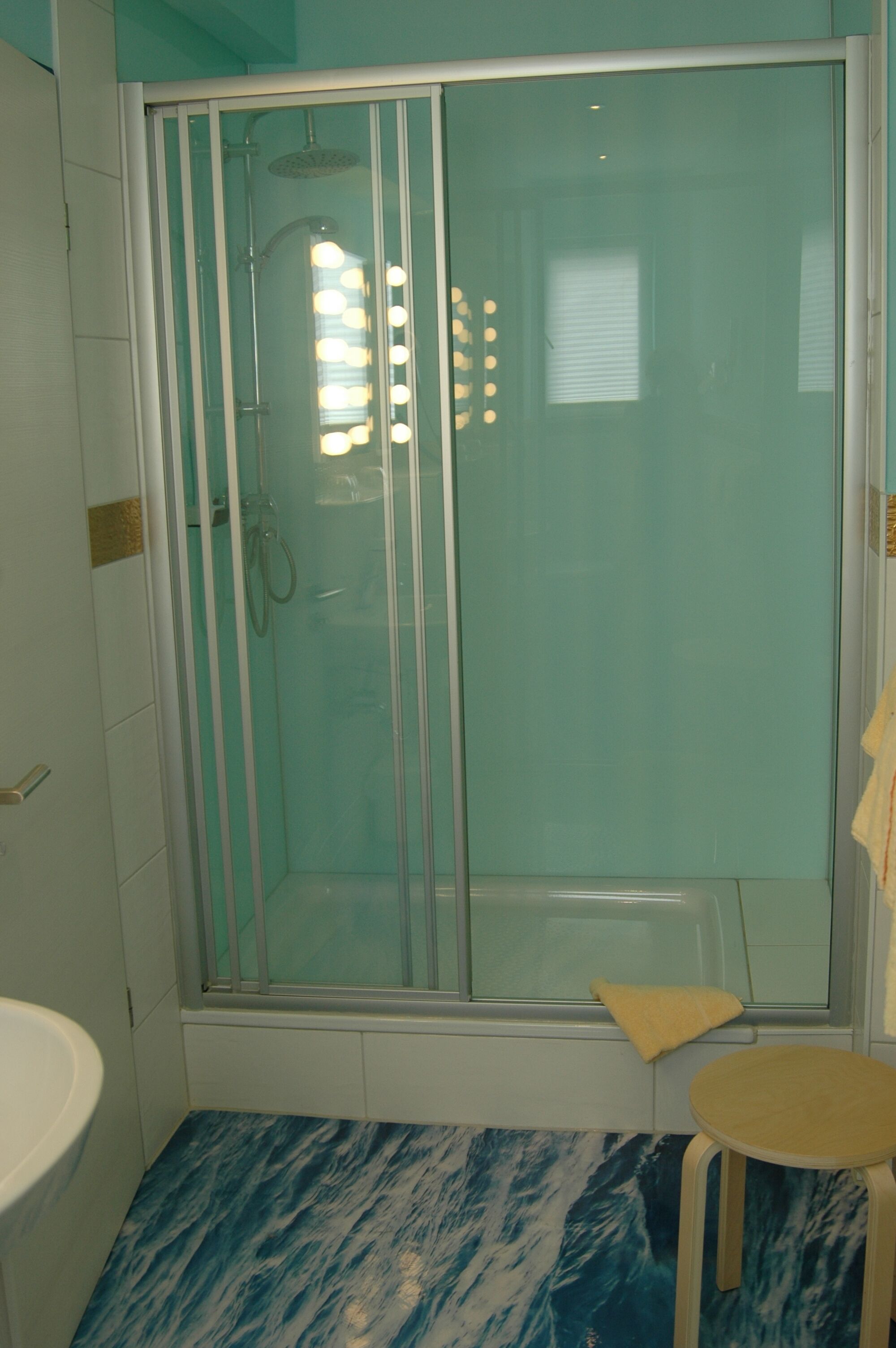A bathroom with a glass-enclosed shower, a white sink, and a marble-patterned floor.