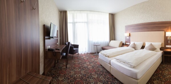 A hotel room with a large bed, a desk with a chair, a television, and a small table. - Vitalhotel König am Park (Bad Mergentheim)