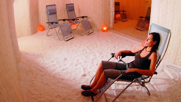 Une salle de spa où une personne se détend dans un fauteuil, entourée de murs recouverts de formations de glace et de quelques autres chaises.