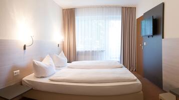 A hotel room with a bed, a desk, a television, and a window with curtains.