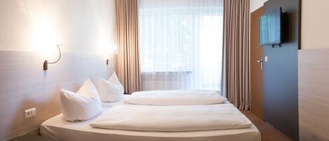 A hotel room with a bed, a desk, a television, and a window with curtains.