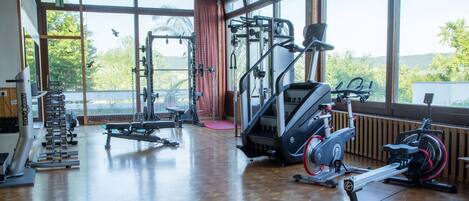 A gym with various exercise equipment, large windows, and a wooden floor.