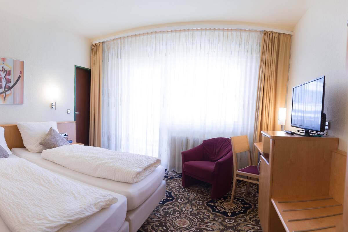 A hotel room with two beds, a desk, a chair, a TV, and a painting on the wall.