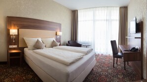 Une chambre d’hôtel avec un grand lit, des tables de chevet, un bureau, une chaise, une télévision et une grande fenêtre avec des rideaux.