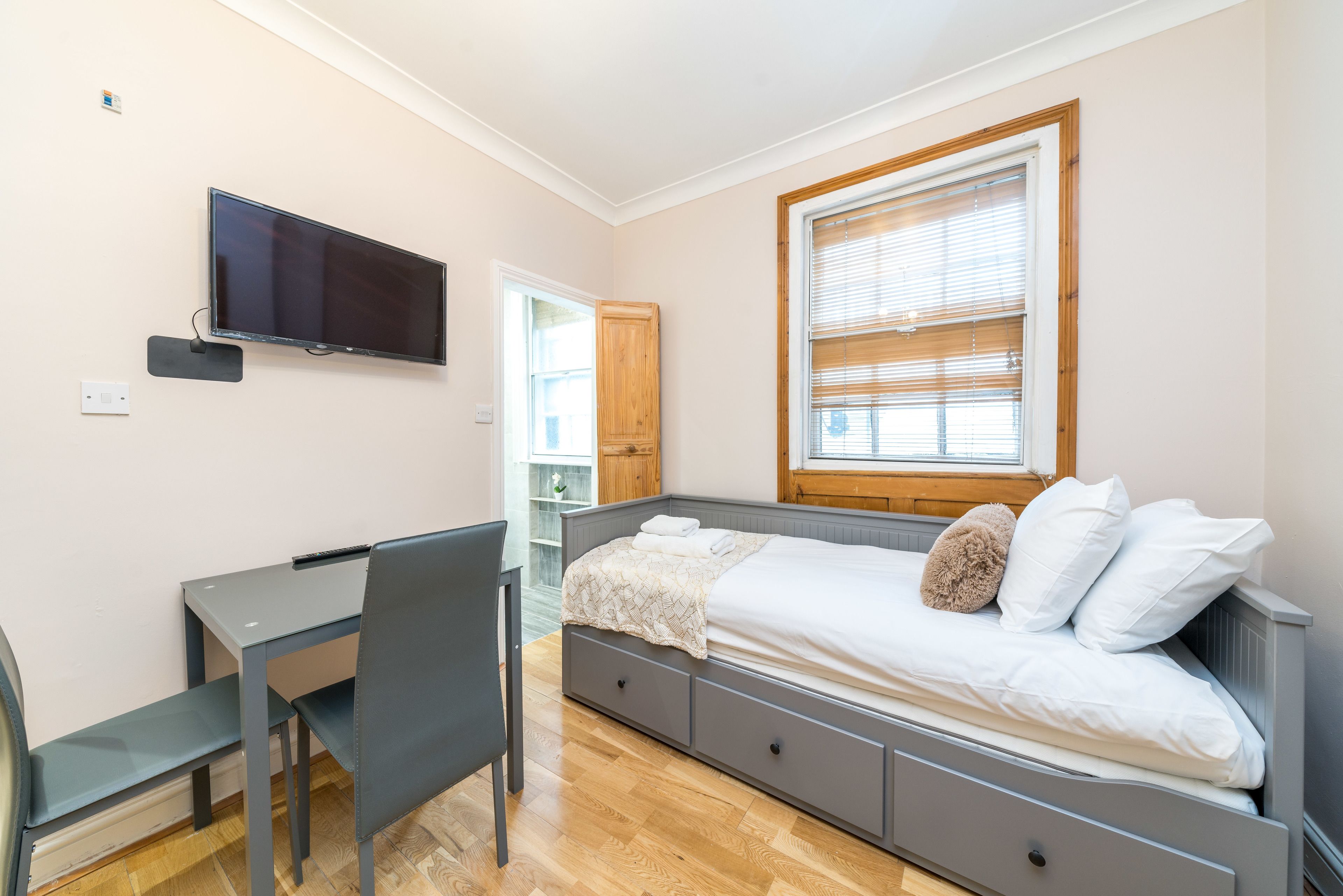 Un dormitorio con cama, escritorio, silla, televisor y ventana.