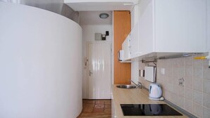 Une cuisine compacte avec des meubles blancs, un évier, une bouilloire et une cuisinière intégrée.