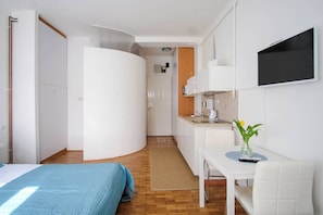 A compact hotel room with a bed, a small kitchenette, a dining area, and a TV mounted on the wall. - Studio Apartment Jedro (Zagreb)