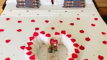 Uma cama com arranjo de pétalas de rosa em formato de coração, um pequeno cesto de presentes e um objeto decorativo no centro.