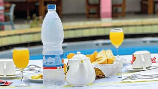 A breakfast setup with a bottle of water, a teapot, toast, and orange juice glasses on a table by a pool. - Imans Hotel Dabou (Dabou)