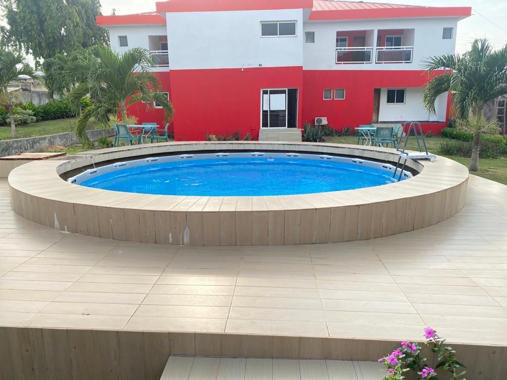 A swimming pool with a wooden deck, surrounded by a red and white building with balconies.