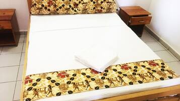 A bed with a patterned bedspread and matching pillow, wooden headboard, two bedside tables, and a tiled floor.
