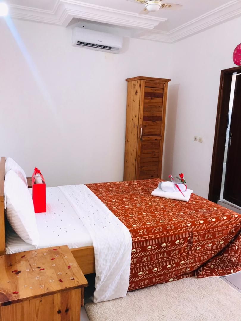 A hotel room with a bed, a wooden wardrobe, a small wooden table, and a red suitcase.
