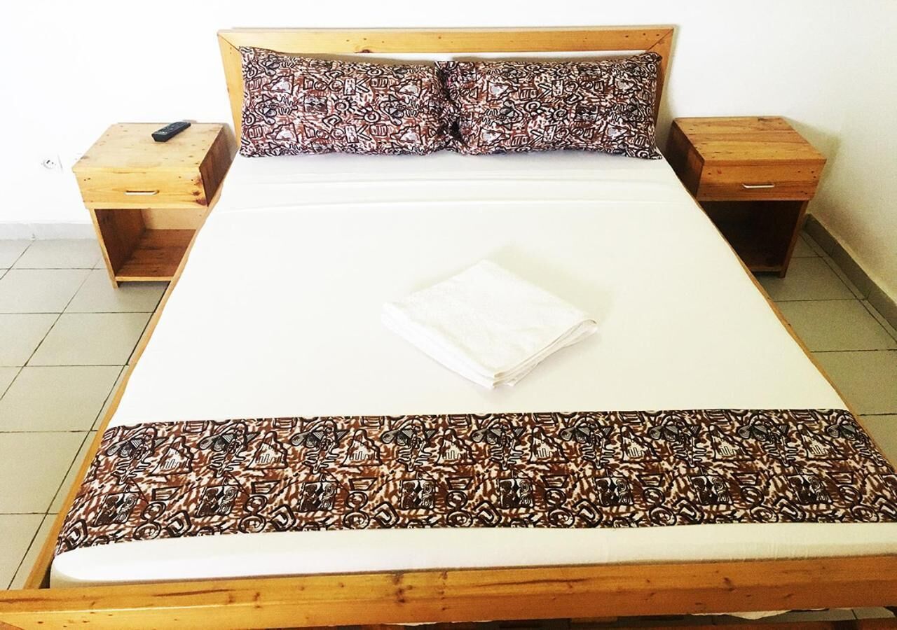 Una cama individual con una colcha y almohadas estampadas, flanqueada por dos mesitas de noche de madera, con un control remoto sobre una de ellas.