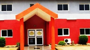 A building with a red facade, a central entrance with a red awning, and two windows on either side of the entrance. - Imans Hotel Dabou (Dabou)