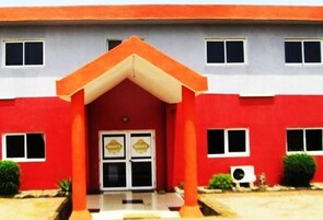 Un edificio con fachada roja, una entrada central con toldo rojo y dos ventanas a cada lado de la entrada.