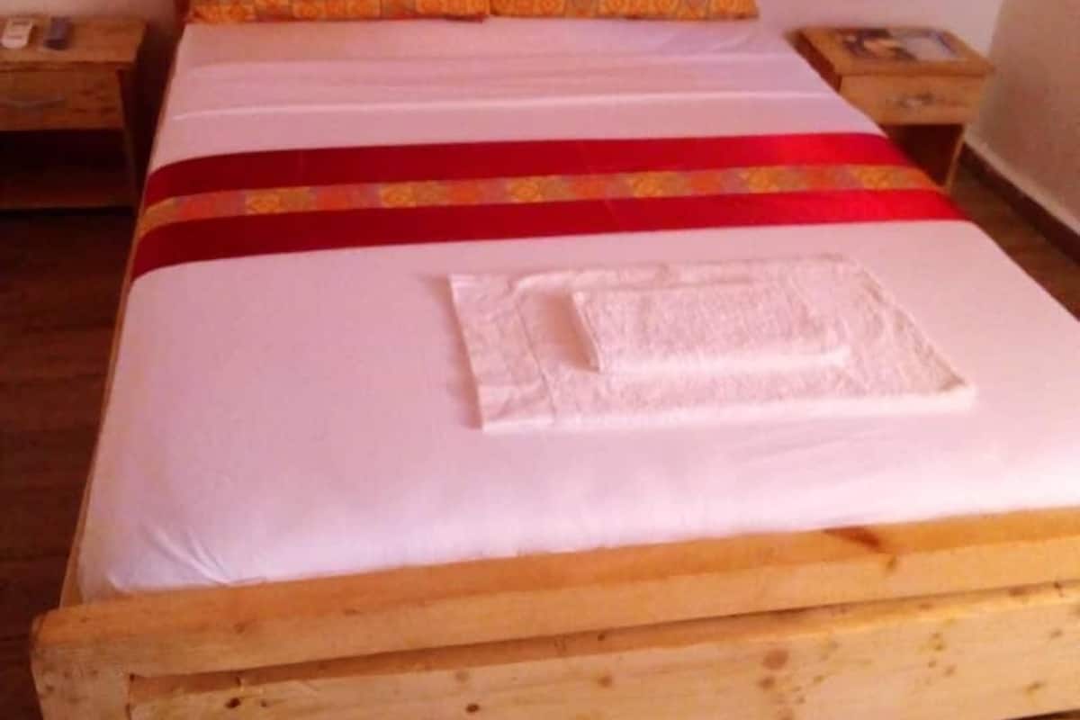 Un lit en bois avec un matelas blanc et des oreillers à motifs rouges et oranges.