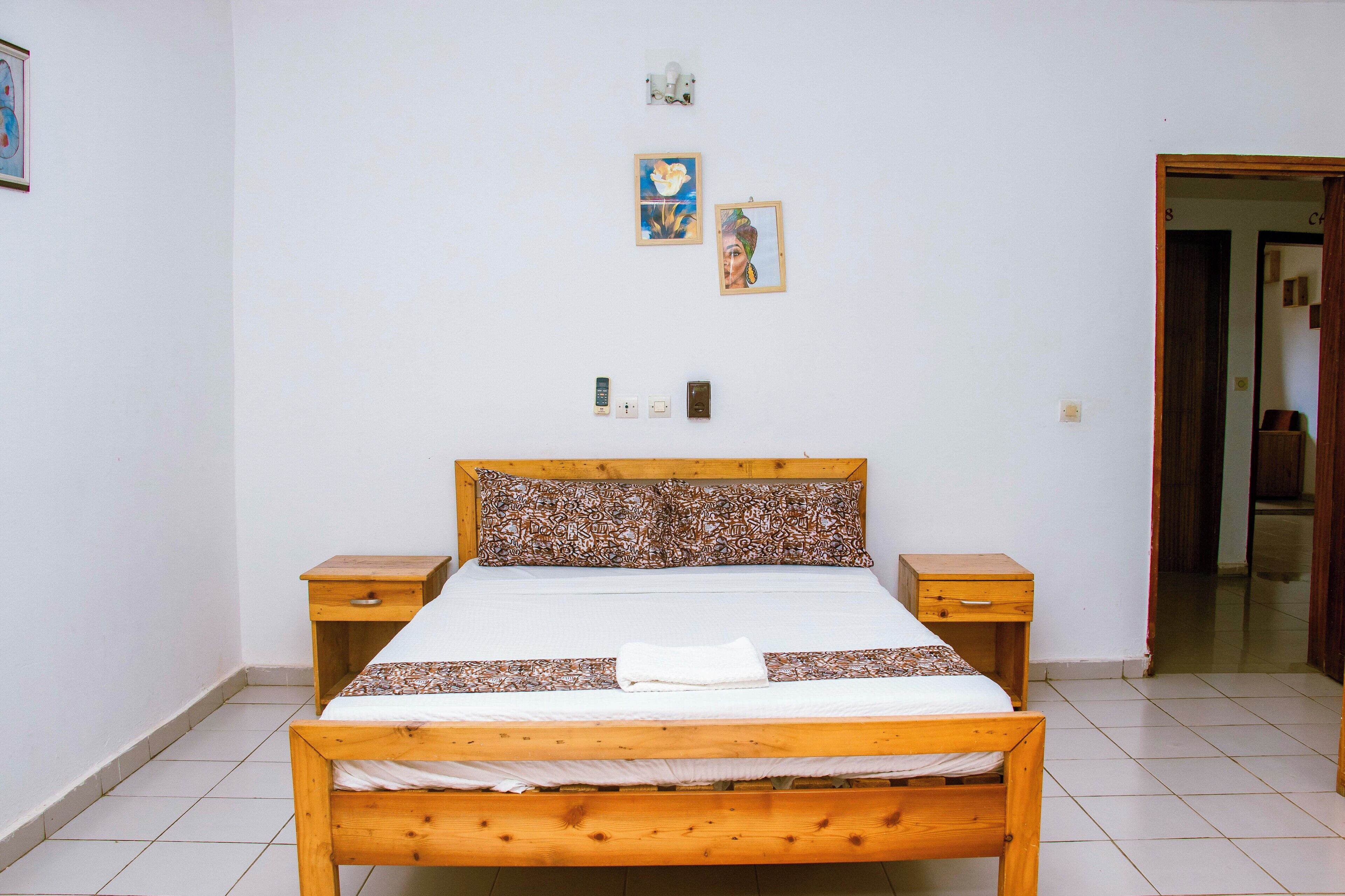A bedroom with a wooden bed, two bedside tables, a wall-mounted light, and two framed pictures.
