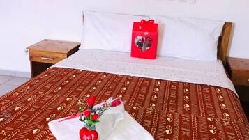 Cama bem arrumada com colcha estampada, mesa de cabeceira pequena e tomada na parede.